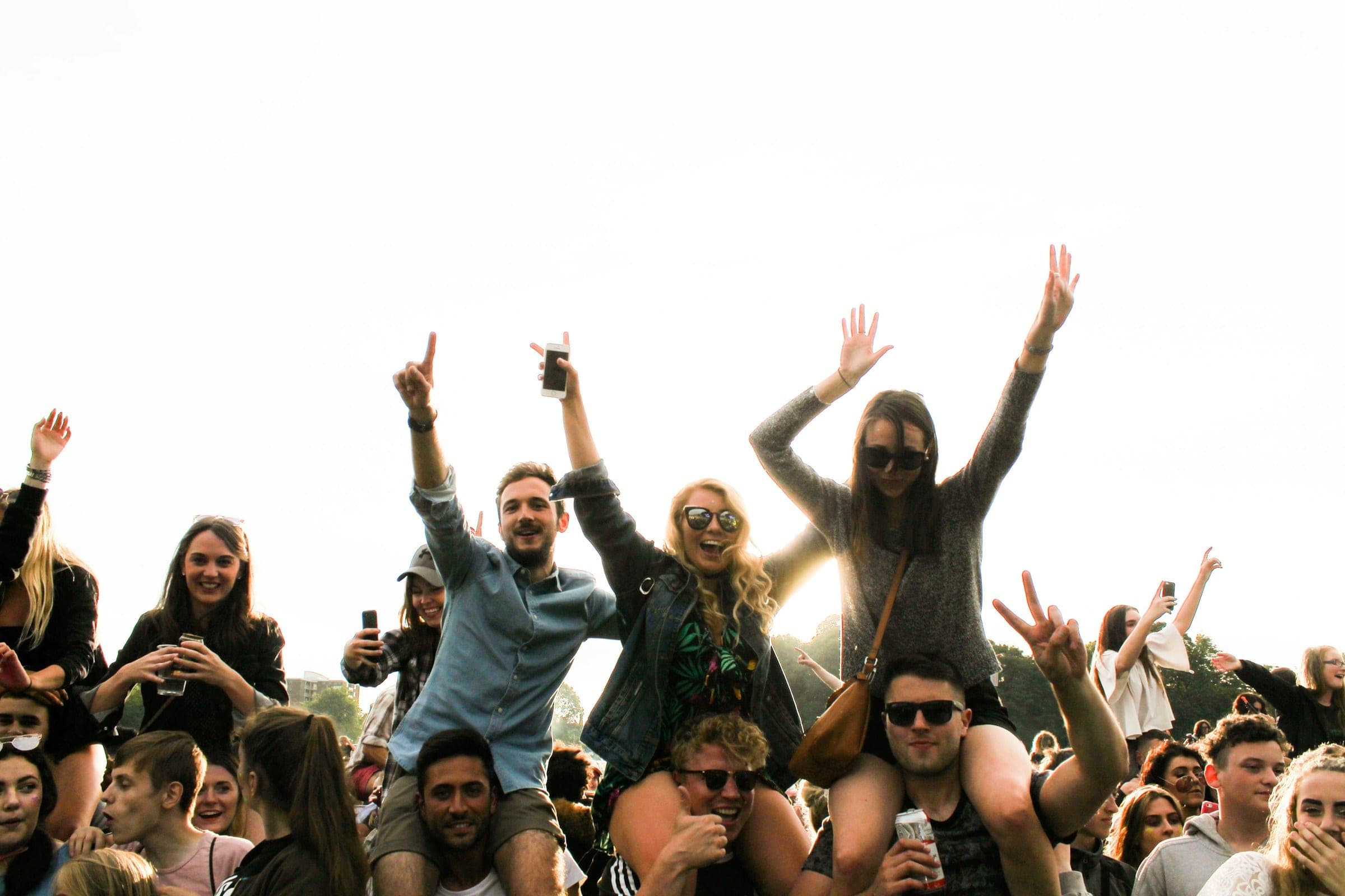 Friends cheering with their arms in the air at an outdoor gig on a bright day