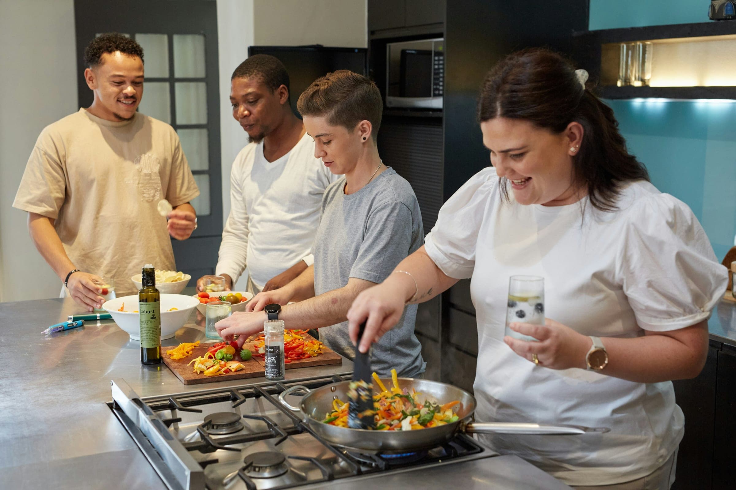 A group of colleagues cooking dinner together in a shared kitchen, smiling
