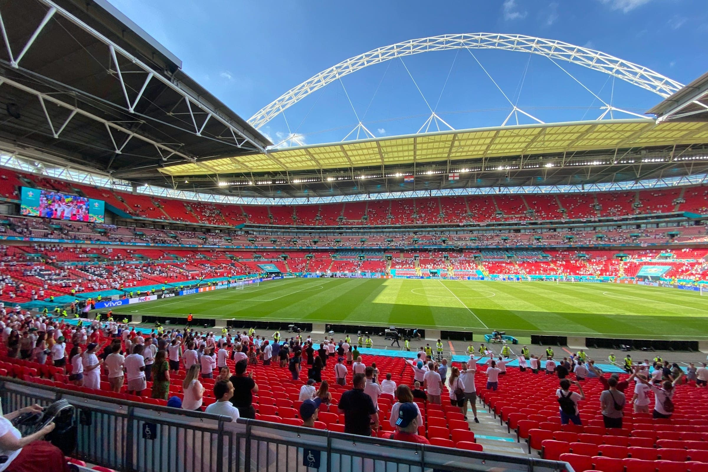 Fans finding their seats inside Wembley Stadium on a sunny day, with the arch against a blue sky